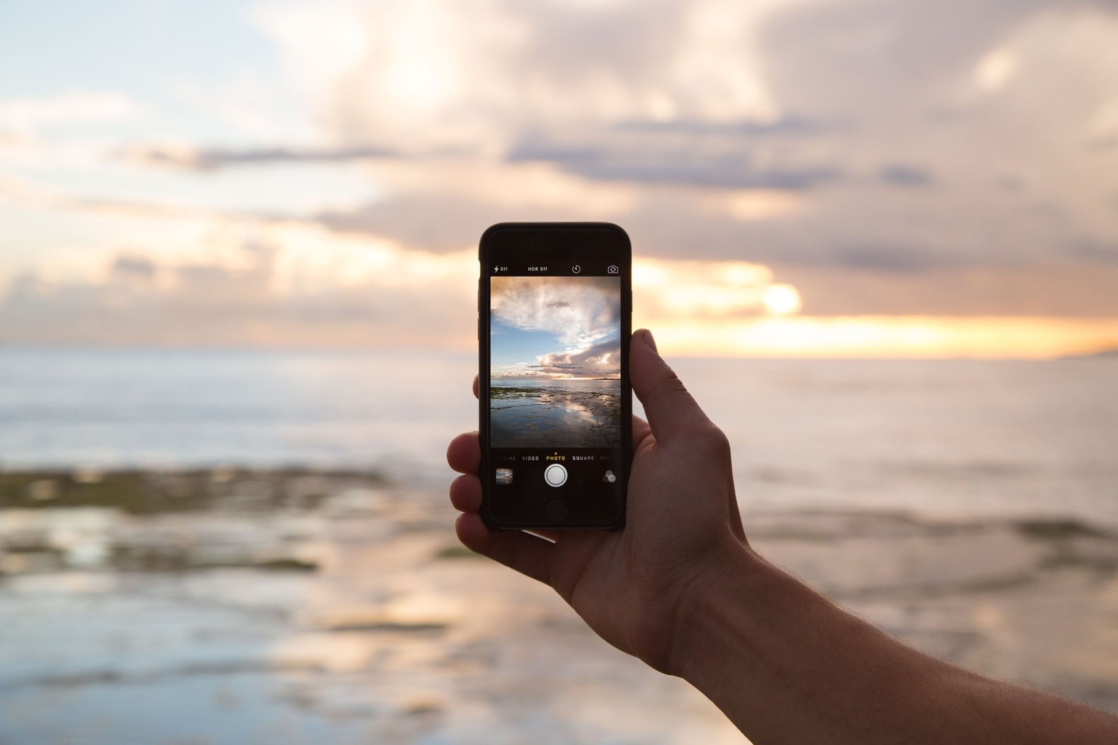 Celular segurado diante do pôr do sol, em fotografia ilustrativa.