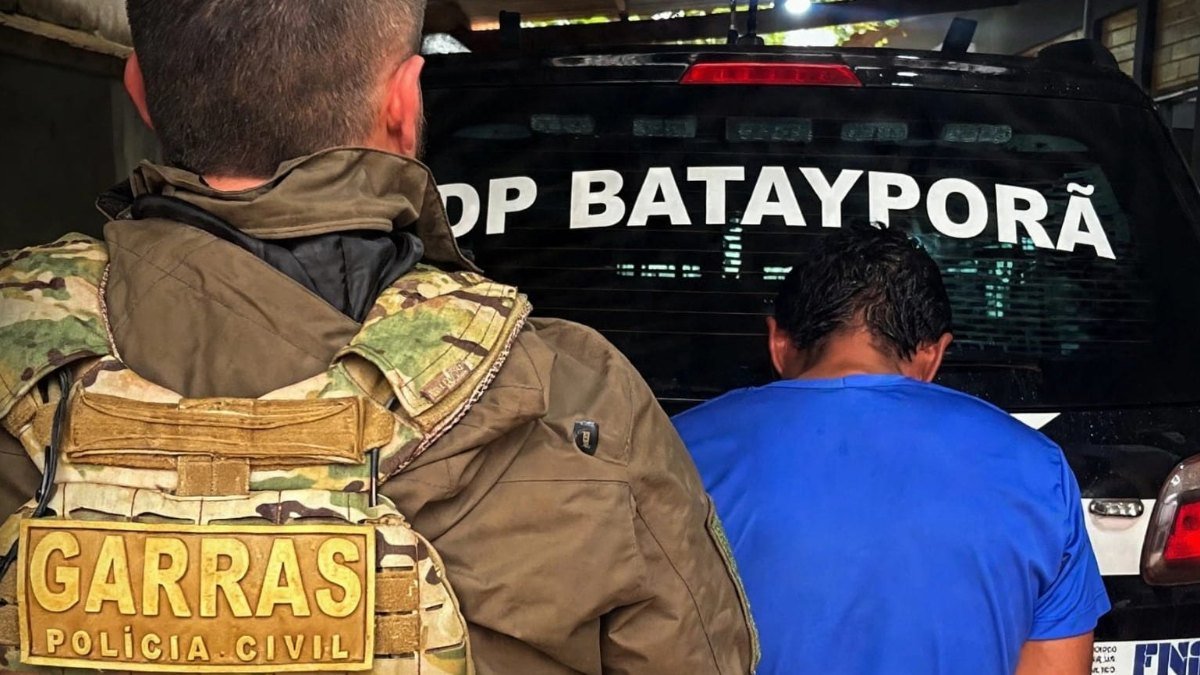 Policial do Garras ao lado de homem preso diante de viatura da Polícia Civil de Batayporã