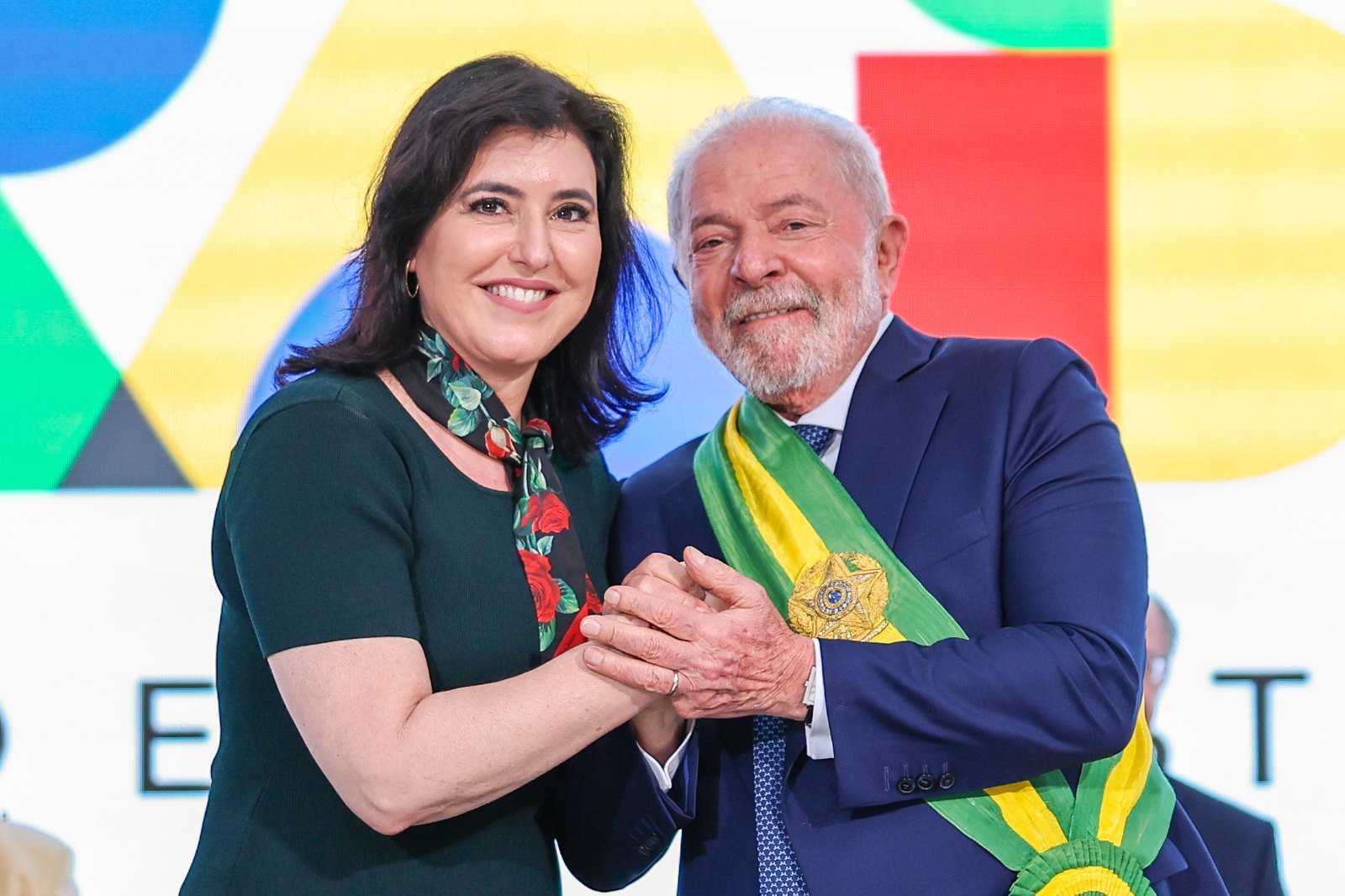 Simone Tebet e o presidente Lula, de mãos dadas e sorrindo, durante a posse dela como ministra do Planejamento, em 1º de janeiro de 2023