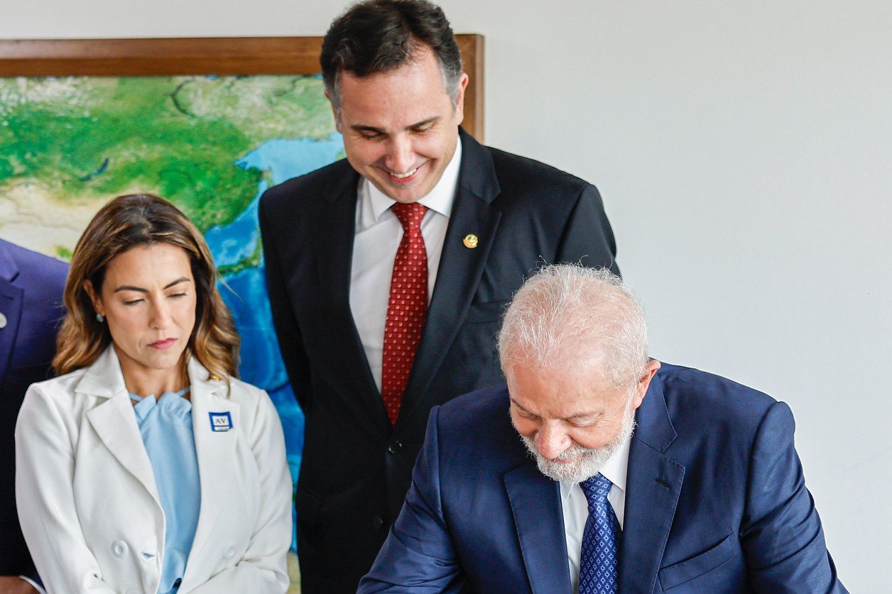 Senadora Soraya Thronicke, de blazer branco, observa o presidente Lula assinar um documento no Palácio do Planalto; ao centro, o então presidente do Senado, Rodrigo Pacheco