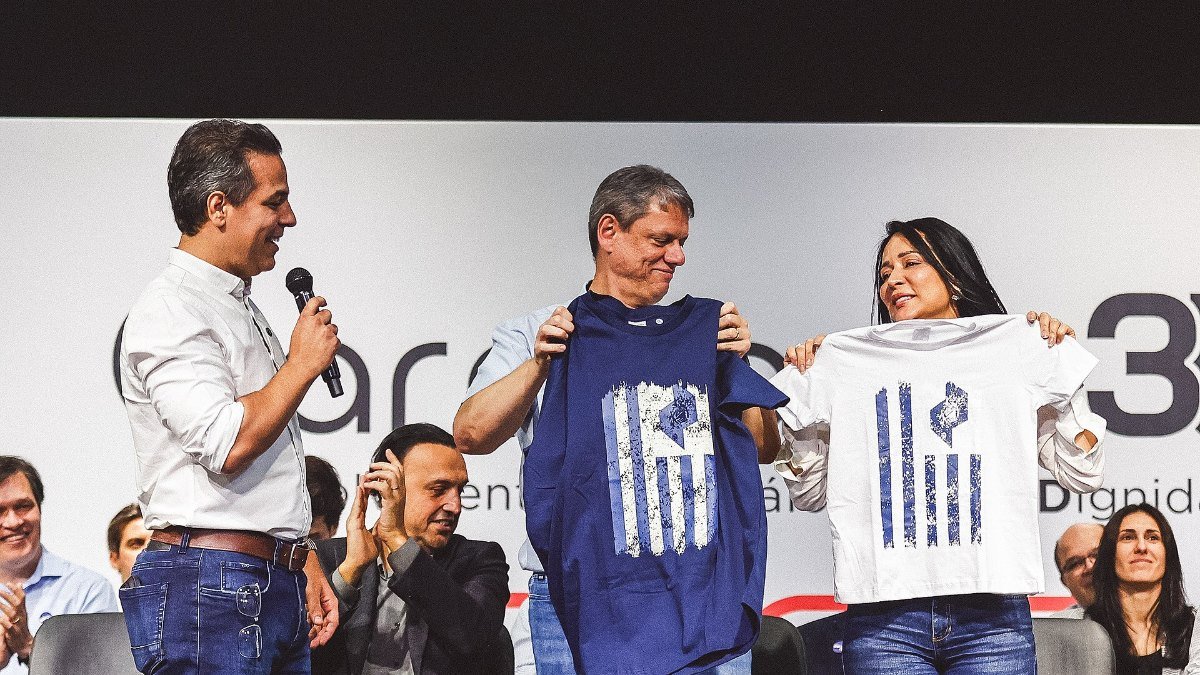 O governador Tarcísio de Freitas, ao centro, segura uma camiseta em evento em Araçatuba